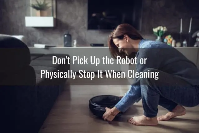 Woman picking up a robotic vacuum for maintenance.