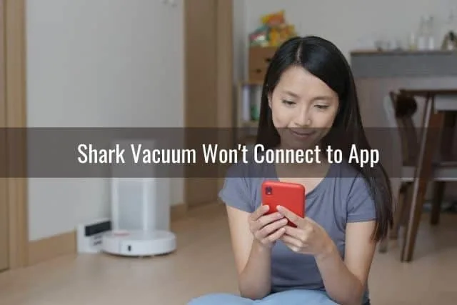 An Asian girl using a red phone to change settings on a white robotic vacuum in the background
