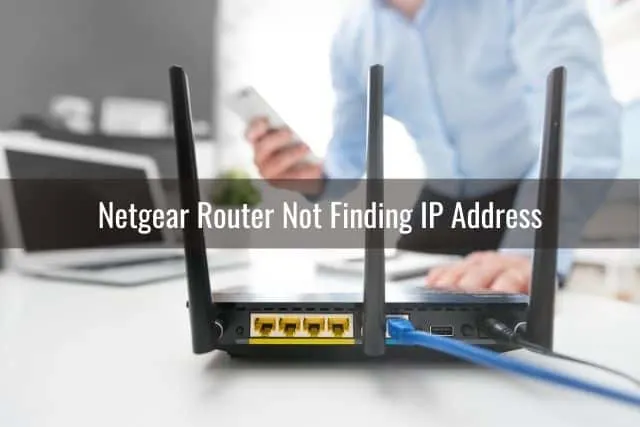 Back of a black wireless router with a man holding a phone in the background