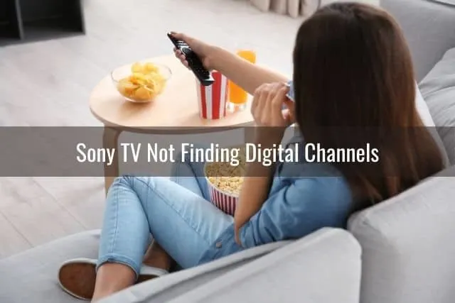 Woman sitting on a sofa pointing remote at TV while eating popcorn