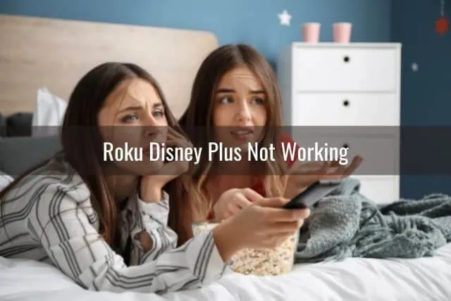 Two female teenagers lying on bed confused with a TV remote