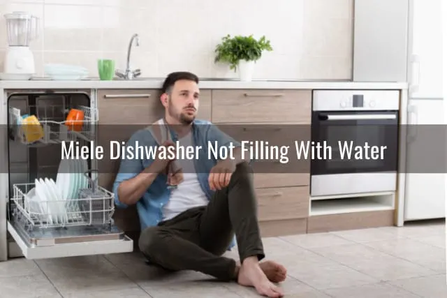 Tired man sitting on the floor behind the dishwasher